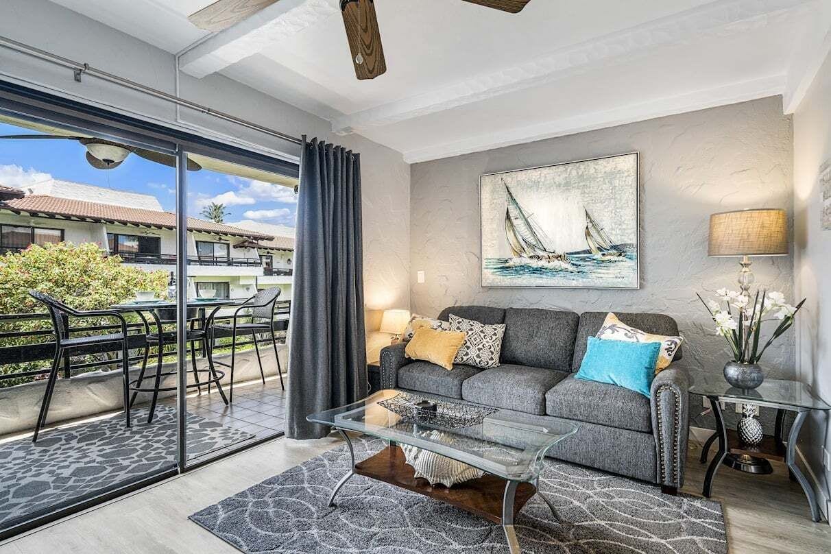 Ein modernes Wohnzimmer mit einem Glastisch, einem grauen Sofa und einem Gemälde eines Segelboots.