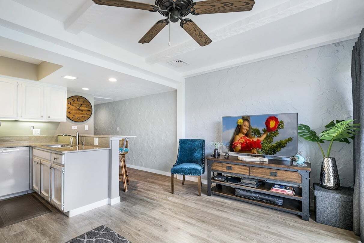 A modern kitchen with white cabinets, a wooden ceiling fan, and a large clock.