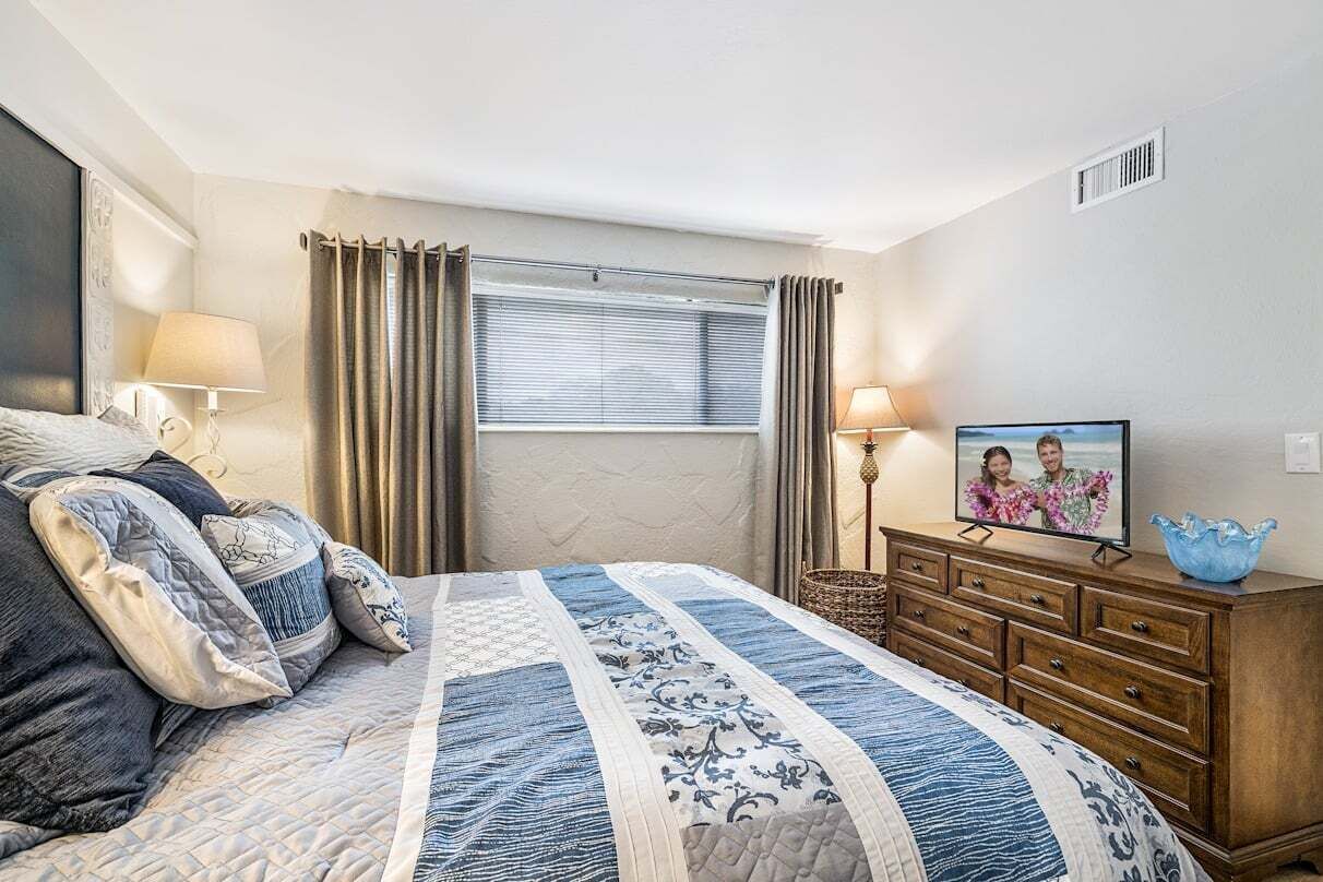 Un dormitorio con cama, cómoda, televisor y ventana con cortinas.