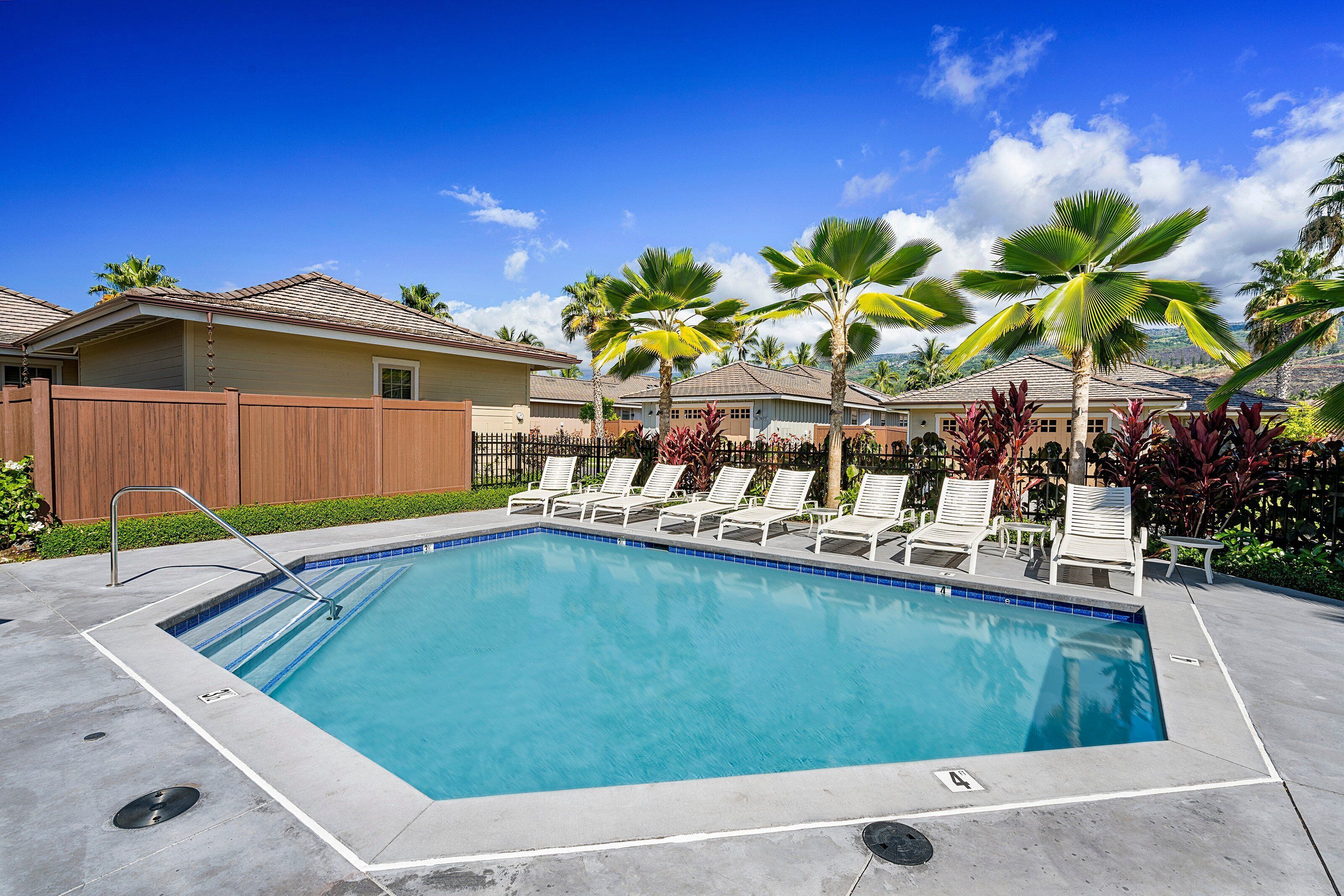 A rectangular pool with a tiled edge, surrounded by lounge chairs and palm trees, with houses in the background.