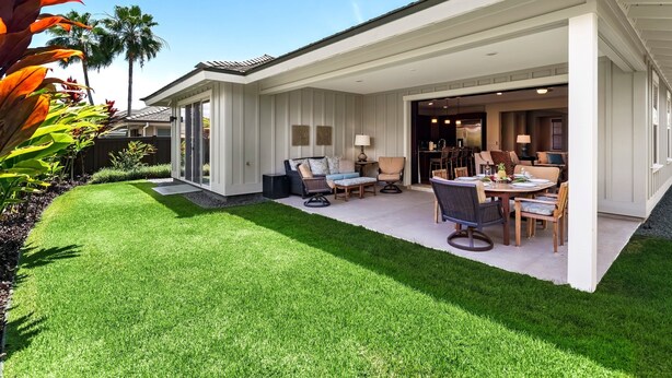 Une maison moderne dotée d’un patio couvert, d’une pelouse et d’un coin repas aménagé avec du mobilier d’extérieur.