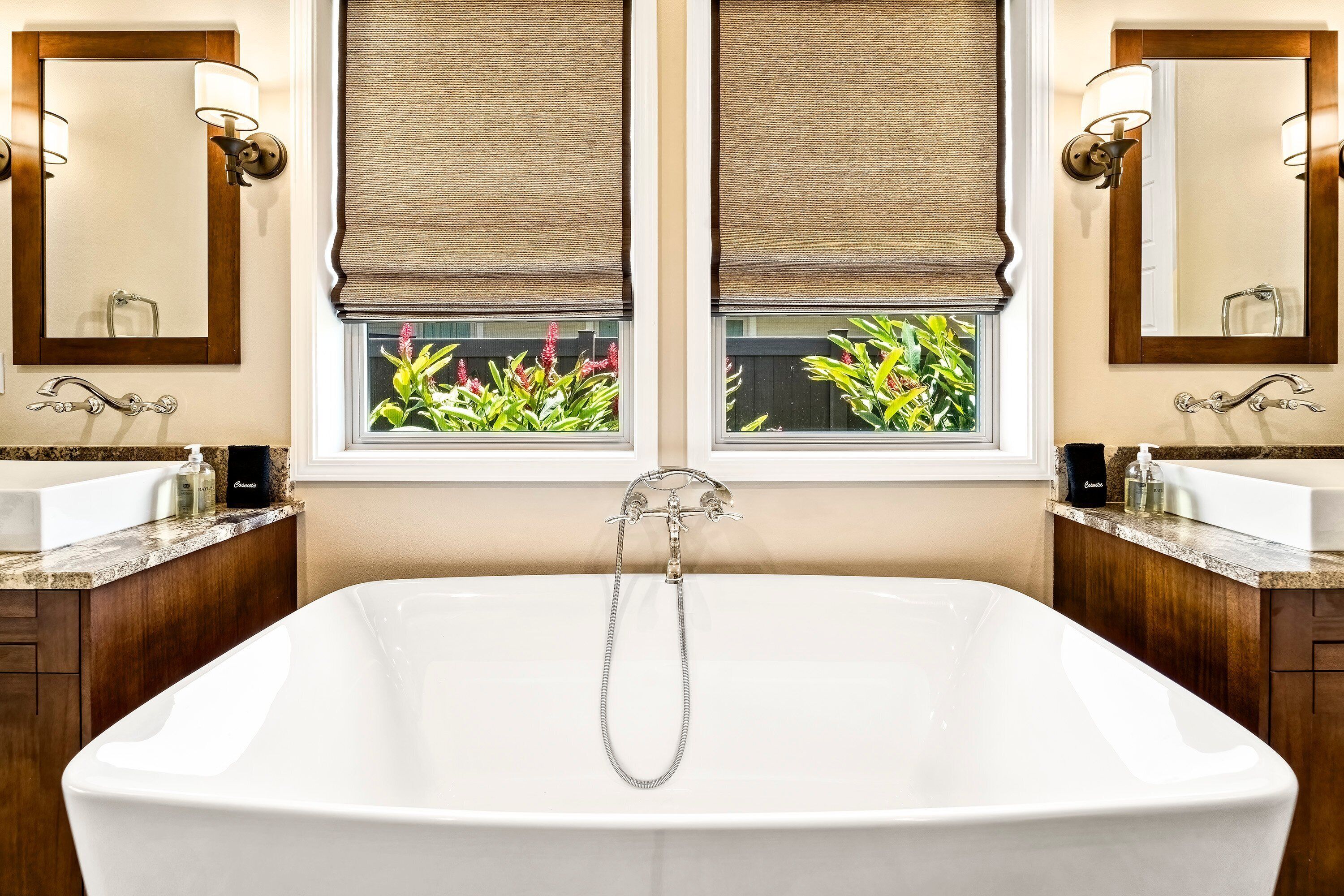 A bathroom with a freestanding bathtub, two sinks, and a window with a view of plants.