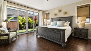 Une chambre dotée d’un grand lit, d’un ventilateur de plafond, d’une table de chevet, d’une chaise et donnant sur un jardin grâce à une porte-fenêtre coulissante.