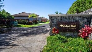 Un quartier résidentiel avec un panneau en pierre indiquant « HOLUA KAI AT KE AUHOU » et une entrée fermée par un portail.