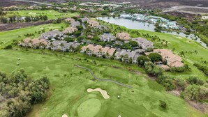 Vista aérea de un campo de golf con edificios residenciales, un lago y montañas a lo lejos.