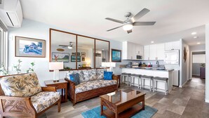 A modern living room with a sofa, coffee table, and a dining area with bar stools. - Ocean Front! - Second Floor With AC & Lanai! - Vrkcv (Kailua-Kona)