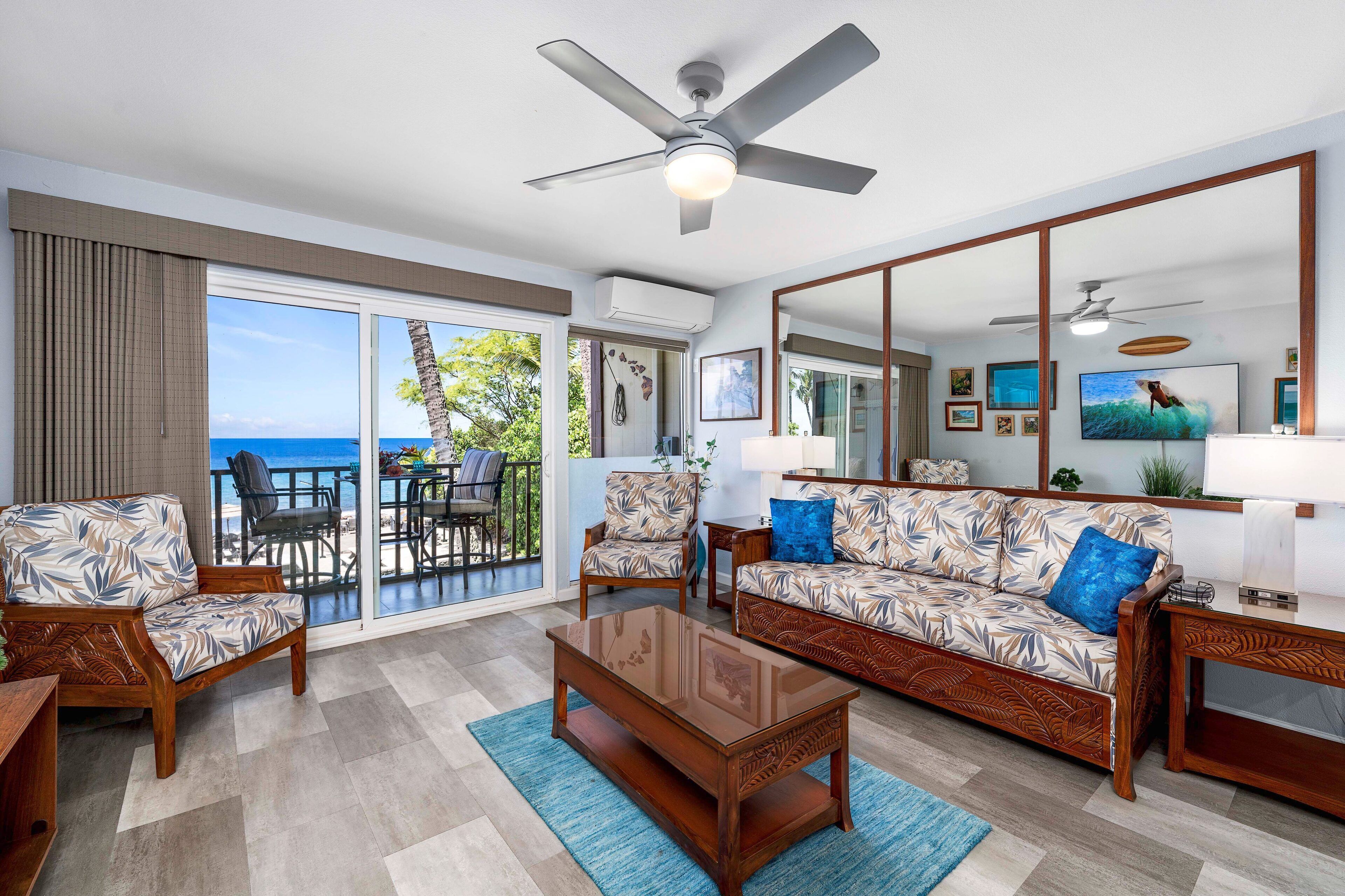 A spacious living area with a balcony overlooking the sea, furnished with a sofa, chairs, and a coffee table.