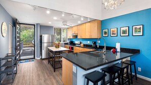 A modern kitchen with wooden cabinets, a black countertop, and a central island with bar stools. - Top Floor With Loft - Ocean and Golf Course Views - AC - Vrkcv (Kailua-Kona)