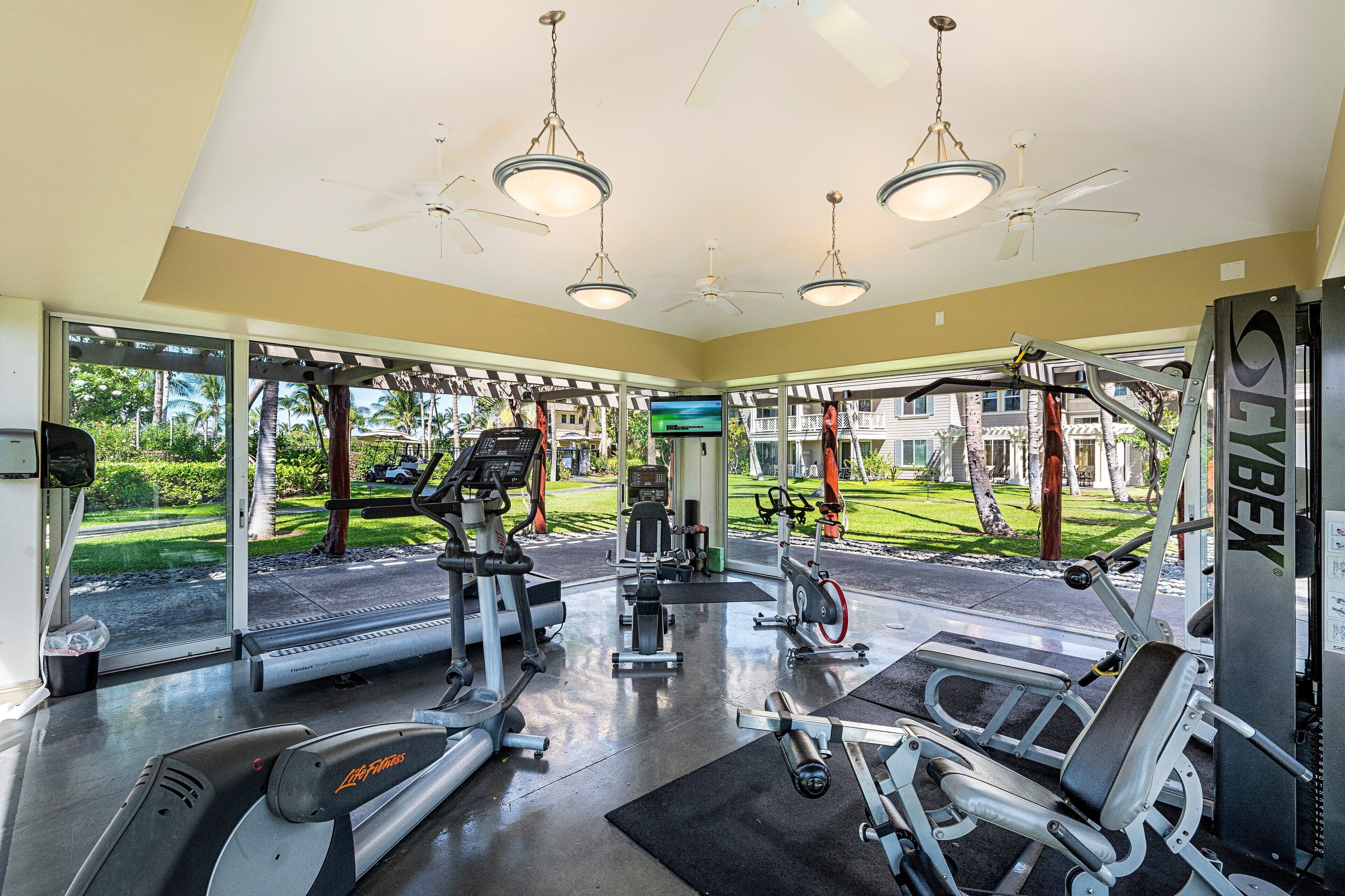 Een sportschool met diverse fitnessapparaten, grote ramen en uitzicht op de omgeving.