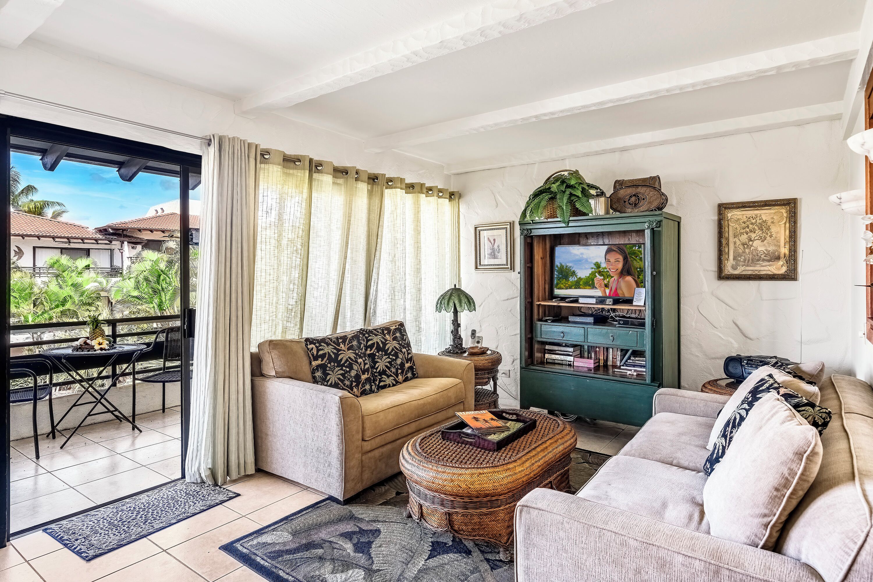 A living room with a sofa, a coffee table, a TV, and a bookshelf. There is a balcony with a table and chairs.
