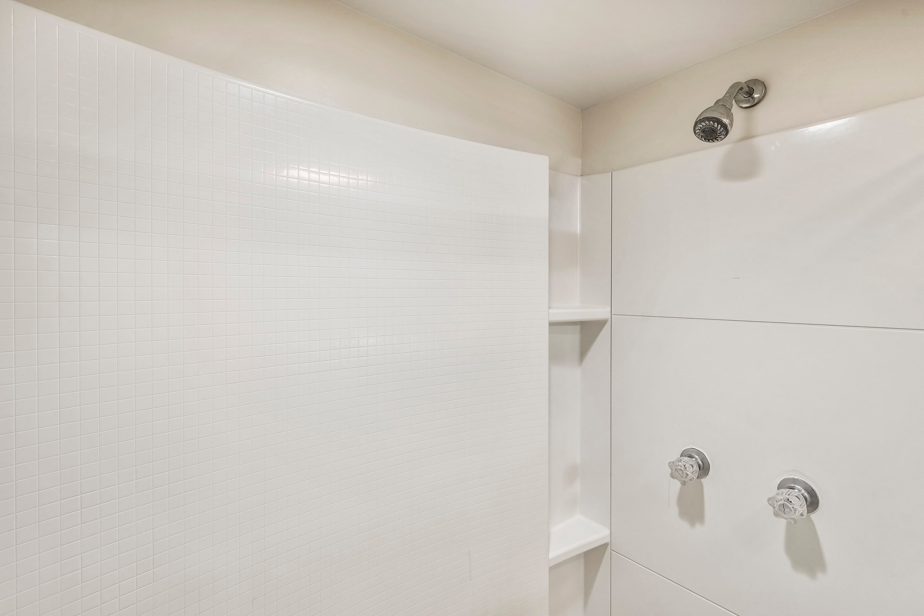 A bathroom with white tiled walls, a shower area, and a toilet.