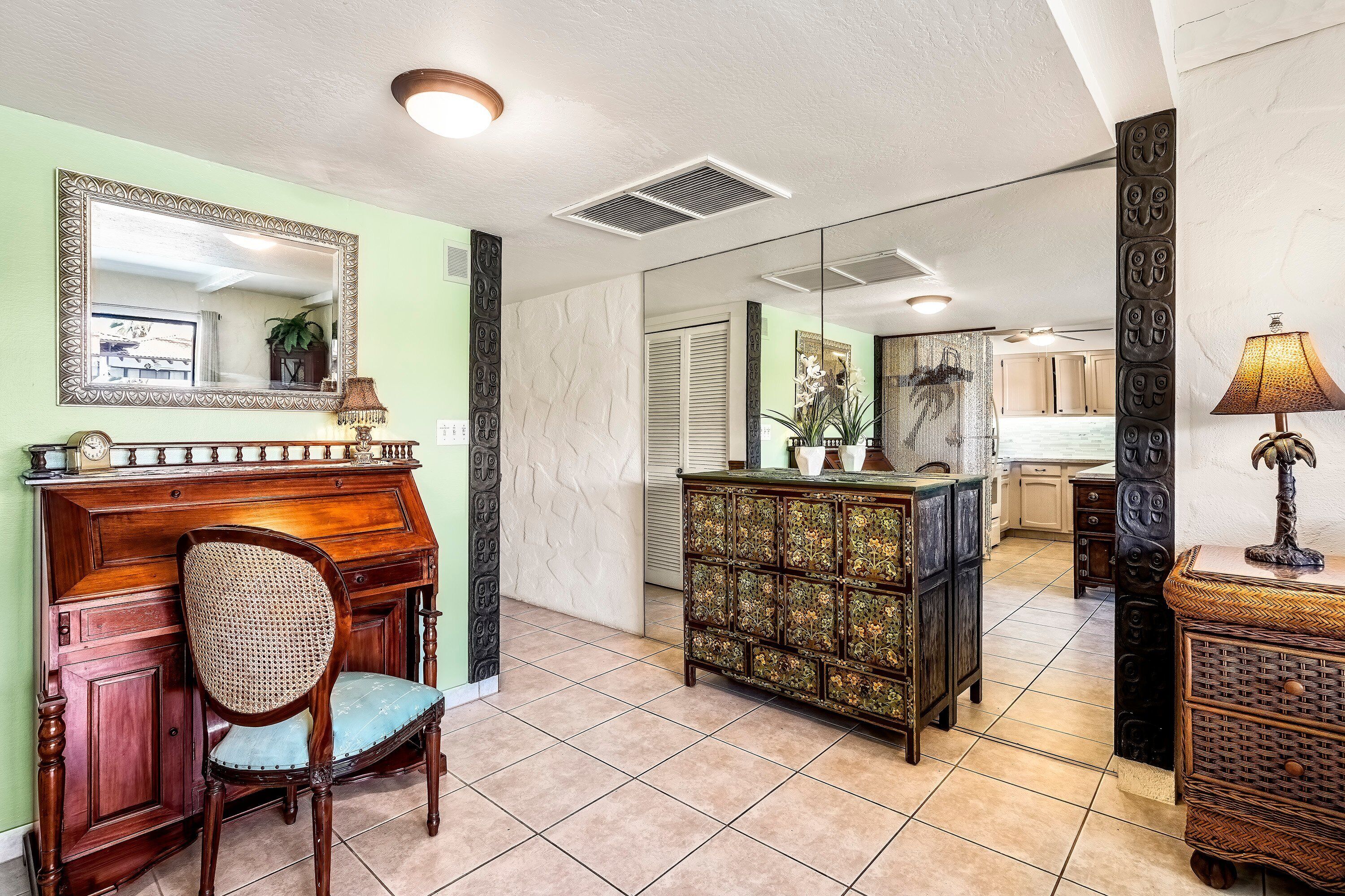 A room with a wooden desk, a chair, a decorative cabinet, and a mirror on the wall.