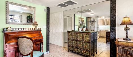 A room with a wooden desk, a chair, a decorative cabinet, and a mirror on the wall.