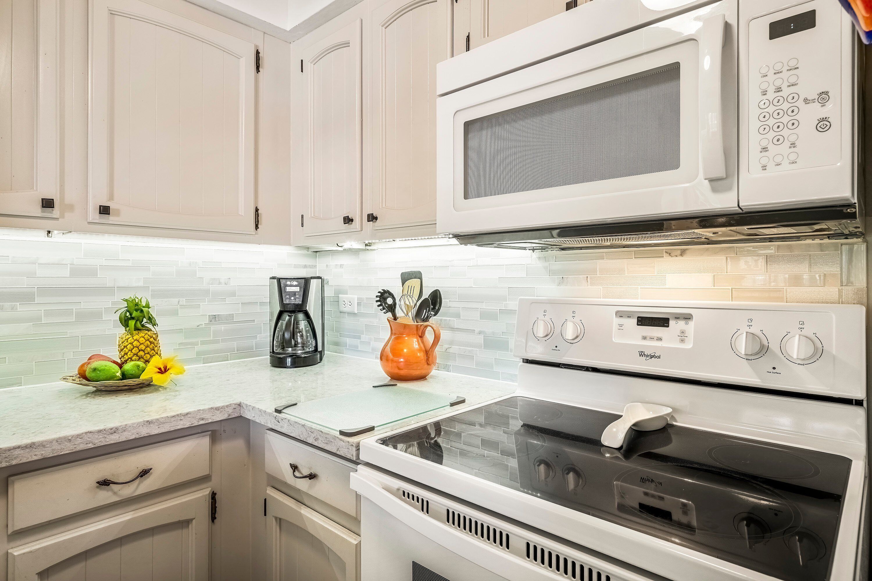 A kitchen with white cabinets, a microwave, a stove, and a coffee maker.