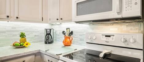 A kitchen with white cabinets, a microwave, a stove, and a coffee maker.