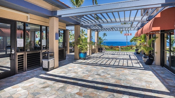 A covered outdoor area with a pool and fitness room, stone flooring, and a view of the ocean.