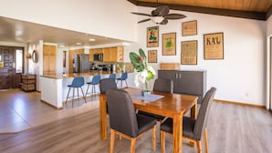 A modern kitchen with wooden cabinets, a central island, and blue chairs. There are framed coffee-related posters on the wall.