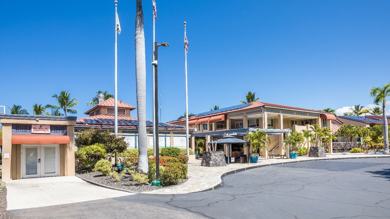 A hotel with a covered outdoor seating area, palm trees, and a clear blue sky.