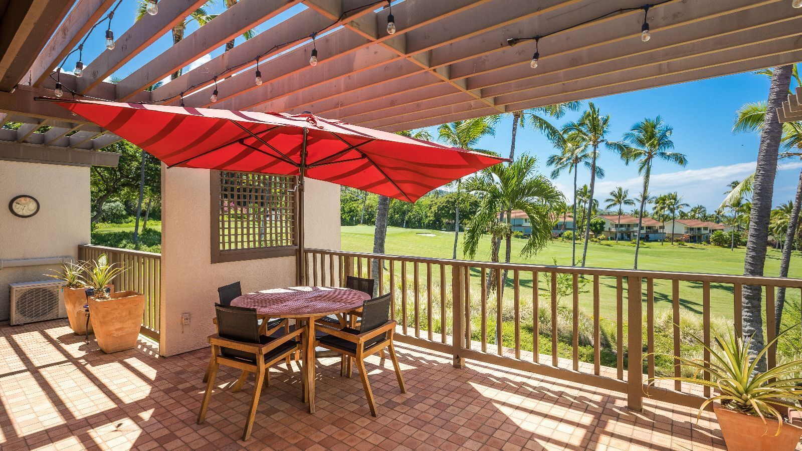 Une terrasse couverte avec une table et des chaises, un parasol rouge et une vue sur un terrain de golf.