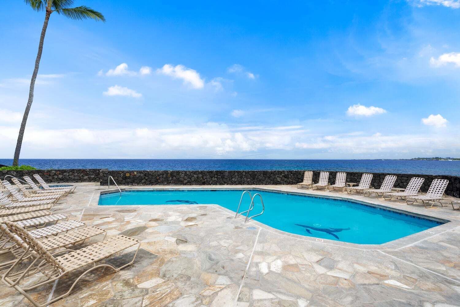 A pool with lounge chairs, a stone deck, and a view of the ocean.
