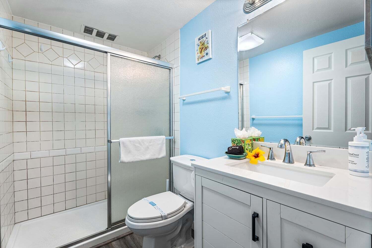 A bathroom with a glass shower enclosure, a white toilet, a sink with a mirror, and a towel rack.