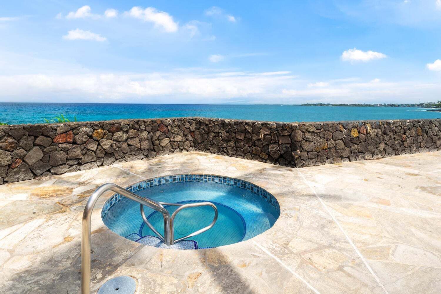 A swimming pool with a stone wall, a metal ladder, and a view of the ocean.