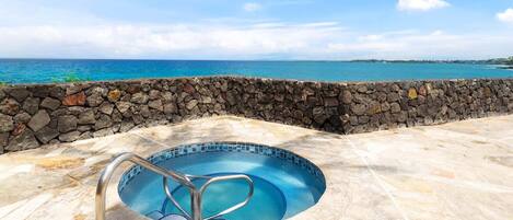 A swimming pool with a stone wall, a metal ladder, and a view of the ocean.