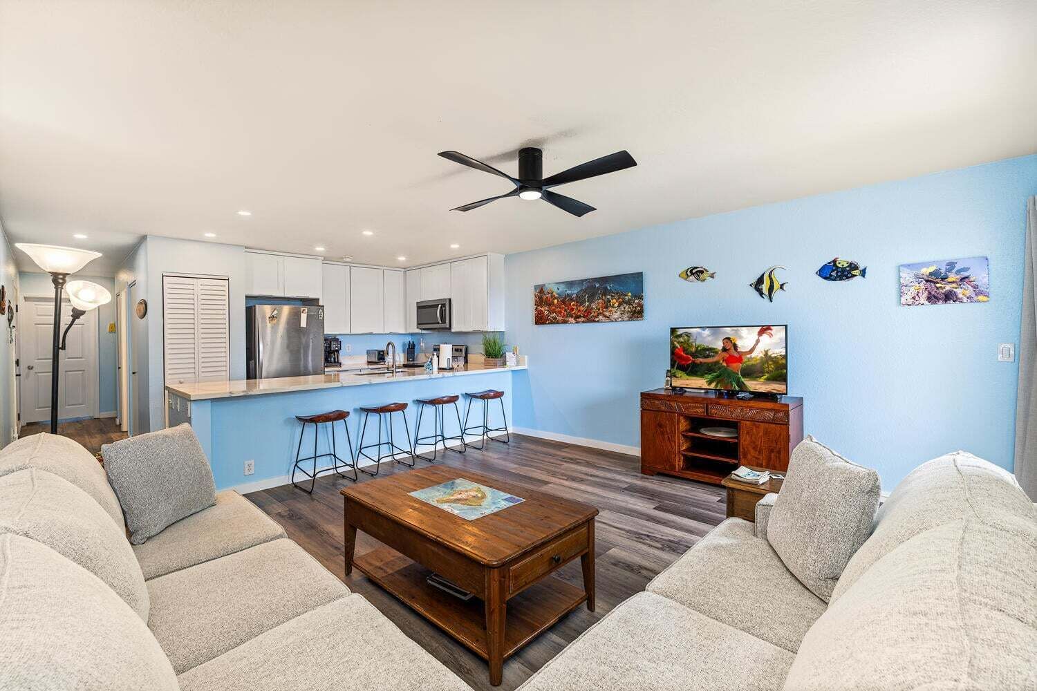 Una sala de estar con una mesa de centro, sofás, televisor y una zona de cocina con taburetes de bar.