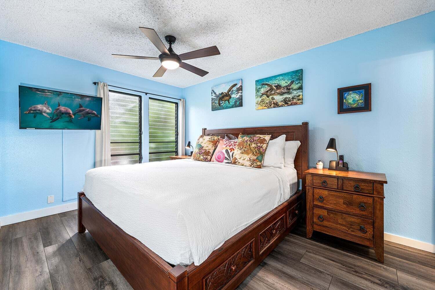 A bedroom with a bed, a nightstand, a ceiling fan, and artwork on the walls.