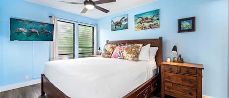 A bedroom with a bed, a nightstand, a ceiling fan, and artwork on the walls.