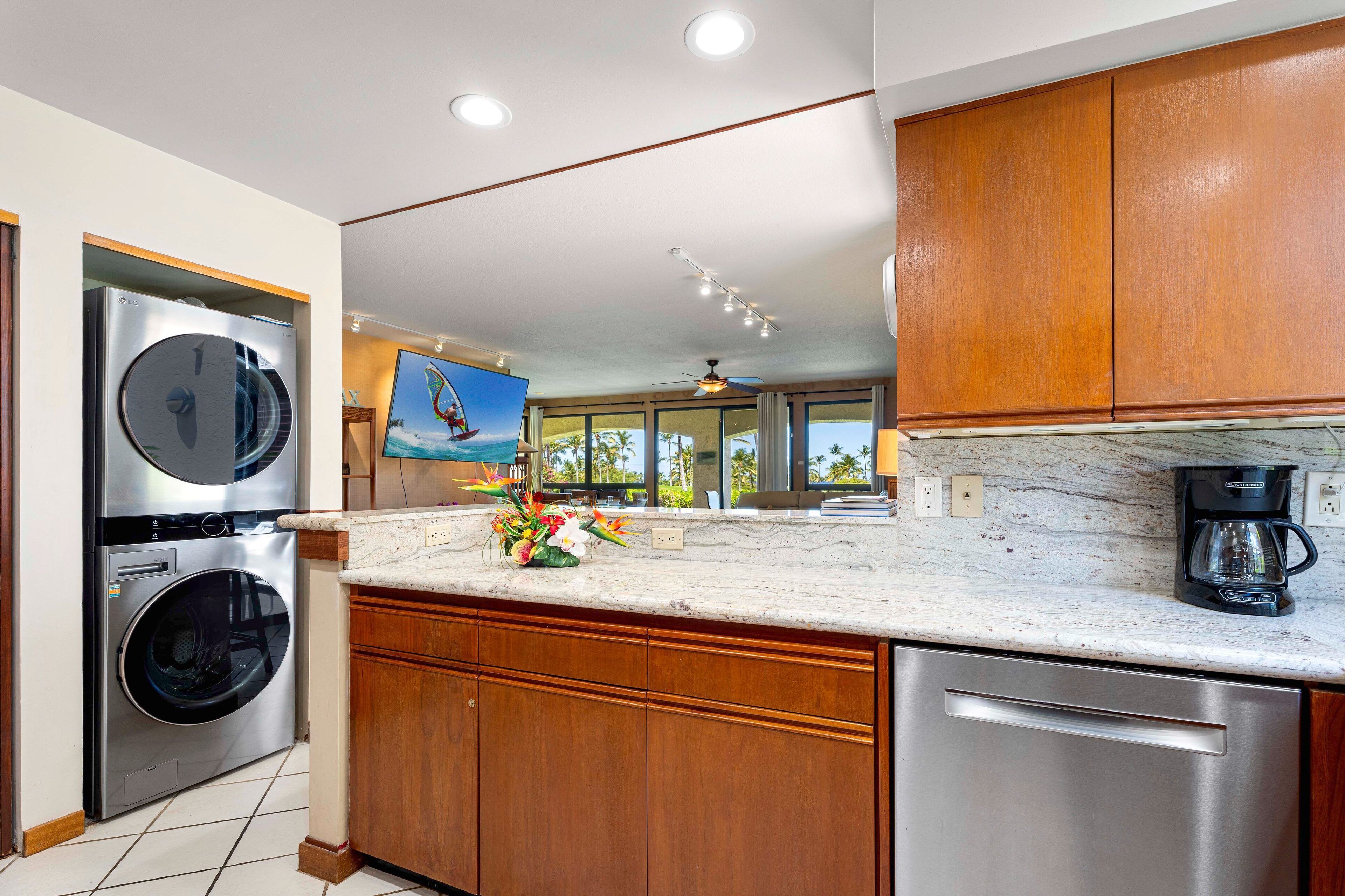 A modern kitchen with stainless steel appliances, wooden cabinets, a marble countertop, and a view of the outdoors.