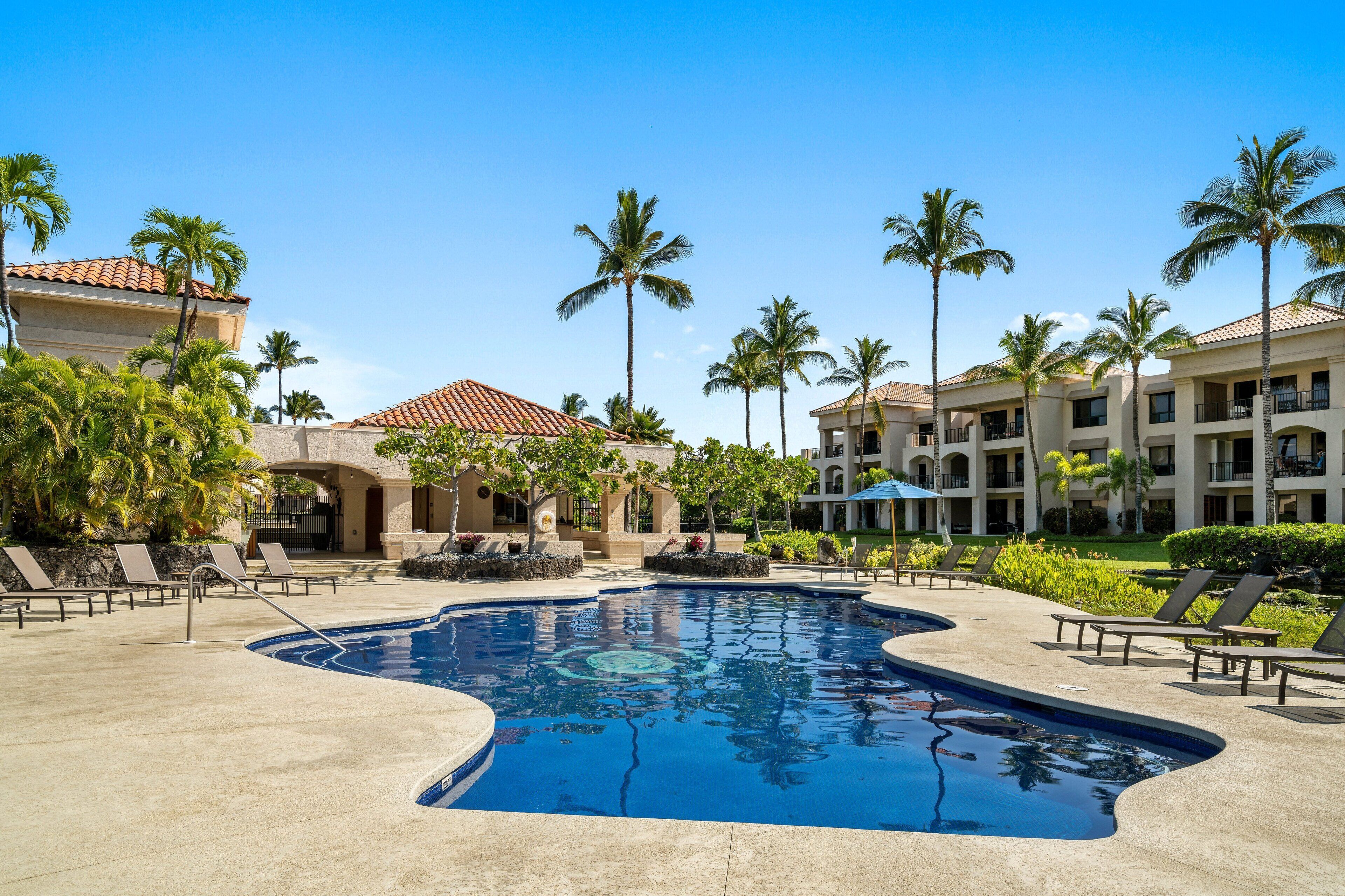 A resort pool area with lounge chairs, palm trees, and a building with a red-tiled roof.