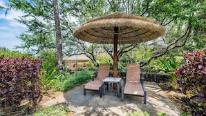 An outdoor seating area with a thatched umbrella, surrounded by lush greenery and a stone pathway. - Beautiful Townhome - Great Location & Amenities - Vrkcv (Kamuela)