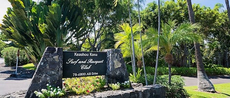 A sign for Keauhou Kona Surf and Racquet Club with a stone wall and tropical landscaping.