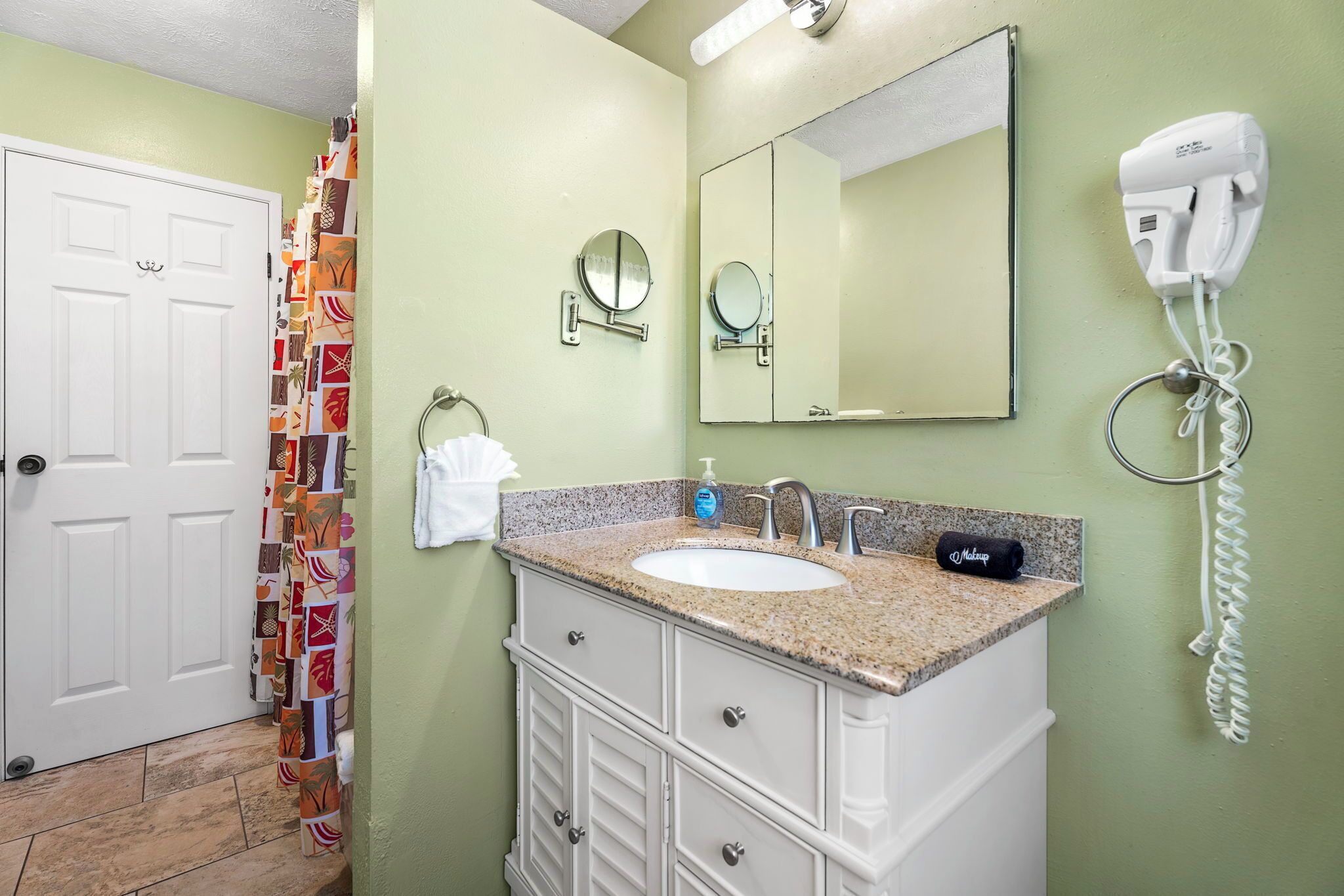 Une salle de bain avec un lavabo blanc, deux miroirs, un sèche-cheveux et un porte-serviettes.