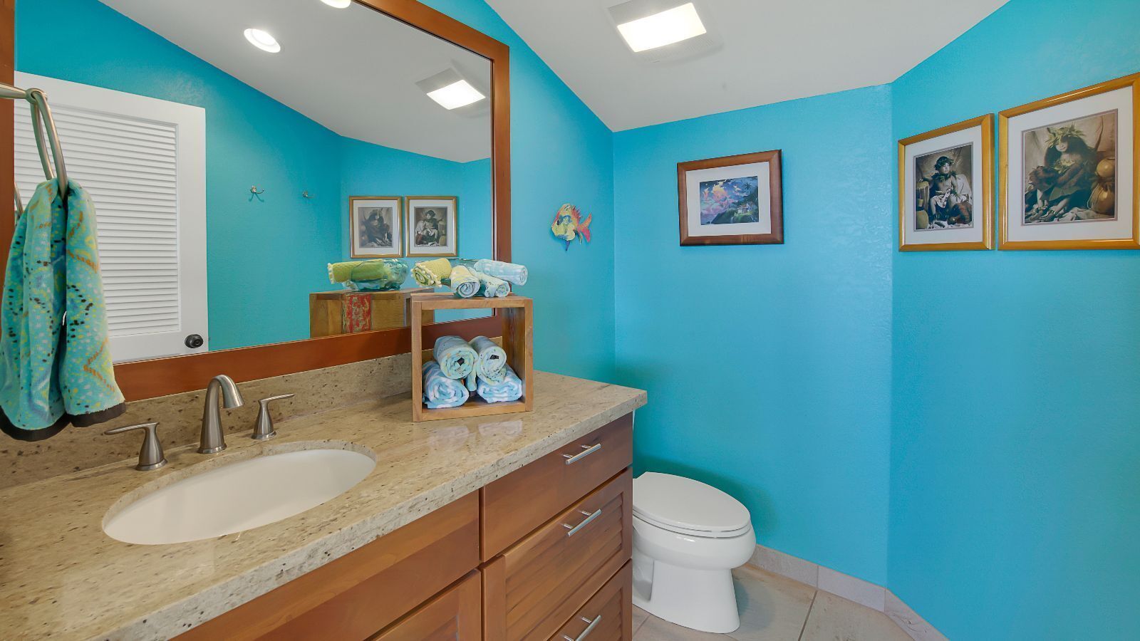 A bathroom with a blue wall, a sink with a mirror, and a toilet.