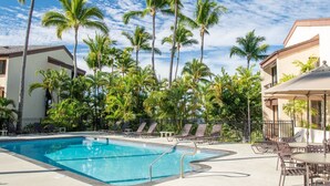 A swimming pool with lounge chairs and umbrellas, surrounded by palm trees and buildings. - Upgraded 2BD Plus Loft - Amazing Golf & Ocean Views - In-unit AC - Vrkcv (Kailua-Kona)