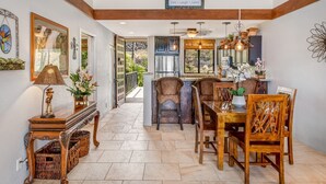 A dining area with a wooden table and chairs, a buffet table, and a view of the outdoors through large windows. - Upgraded 2BD Plus Loft - Amazing Golf & Ocean Views - In-unit AC - Vrkcv (Kailua-Kona)