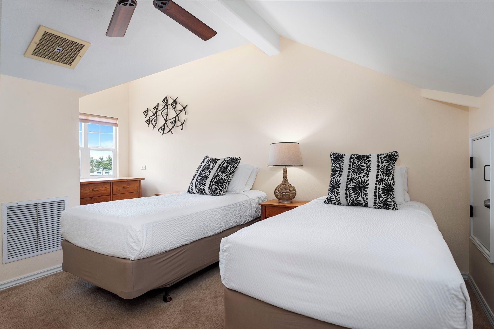 A bedroom with two single beds, a wooden nightstand, a wall-mounted lamp, and a window with blinds.