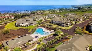 A residential area with a swimming pool, houses with sloped roofs, and a view of the ocean. - Concierge Included - Ocean View - Walk to Beach - Central AC - Vrkcv (Kailua-Kona)
