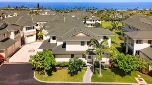 A residential area with houses featuring sloped roofs, a well-maintained lawn, and a view of the ocean. - Concierge Included - Ocean View - Walk to Beach - Central AC - Vrkcv (Kailua-Kona)