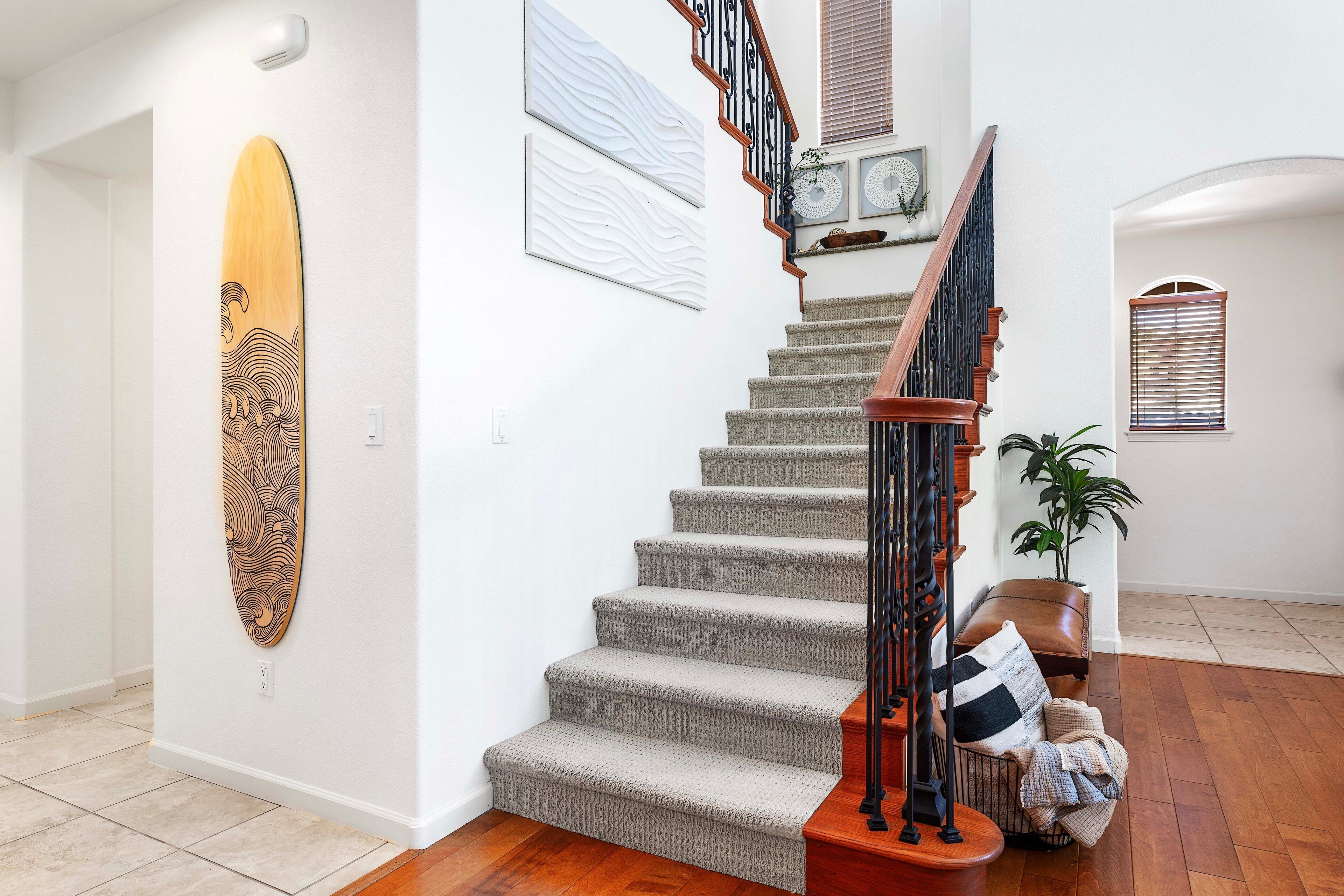 A staircase with carpeted steps and a wooden handrail, leading to a landing with a potted plant and a bench.