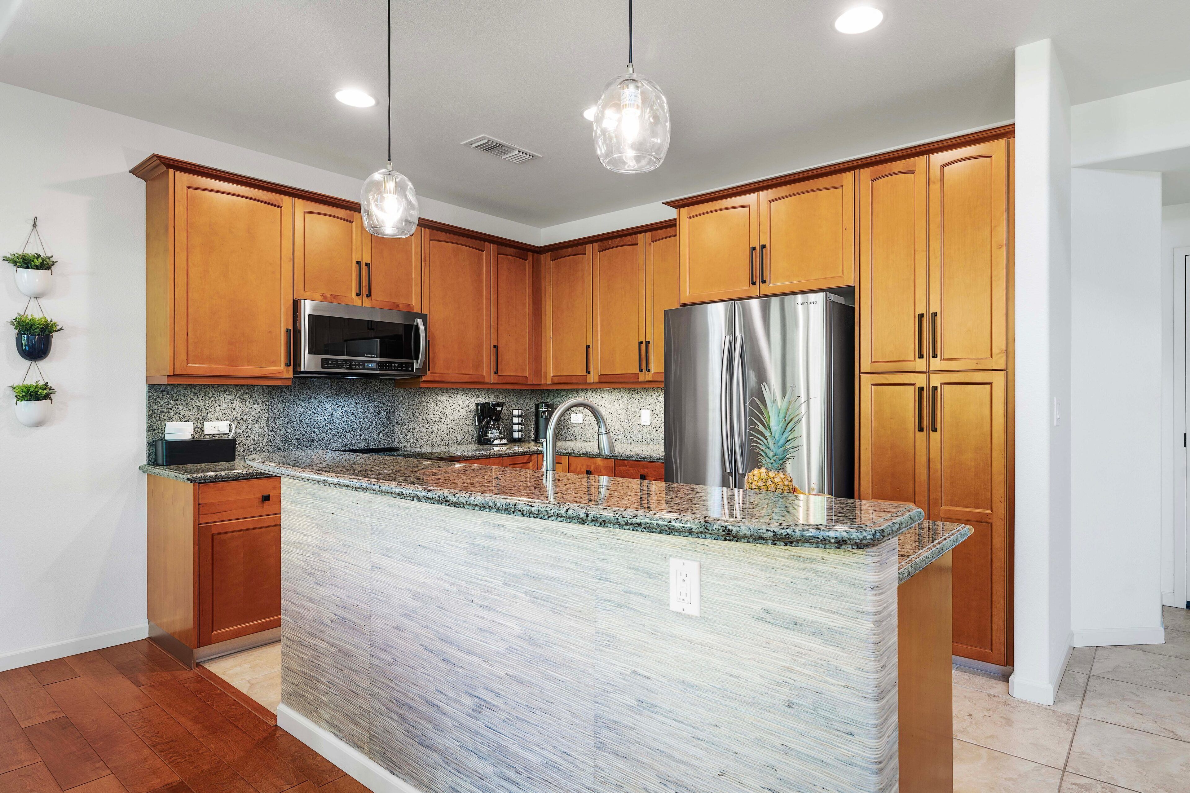 Una cocina moderna con armarios de madera, encimera de granito, electrodomésticos de acero inoxidable e iluminación colgante.