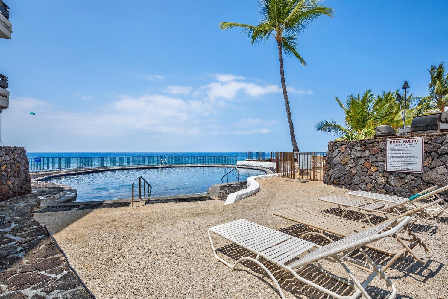 A pool area with lounge chairs, a palm tree, and a sign indicating pool rules.