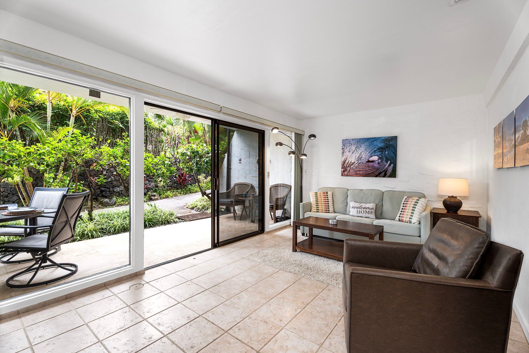 A modern living room with a sliding glass door leading to a garden, a sofa, a coffee table, and a painting on the wall.