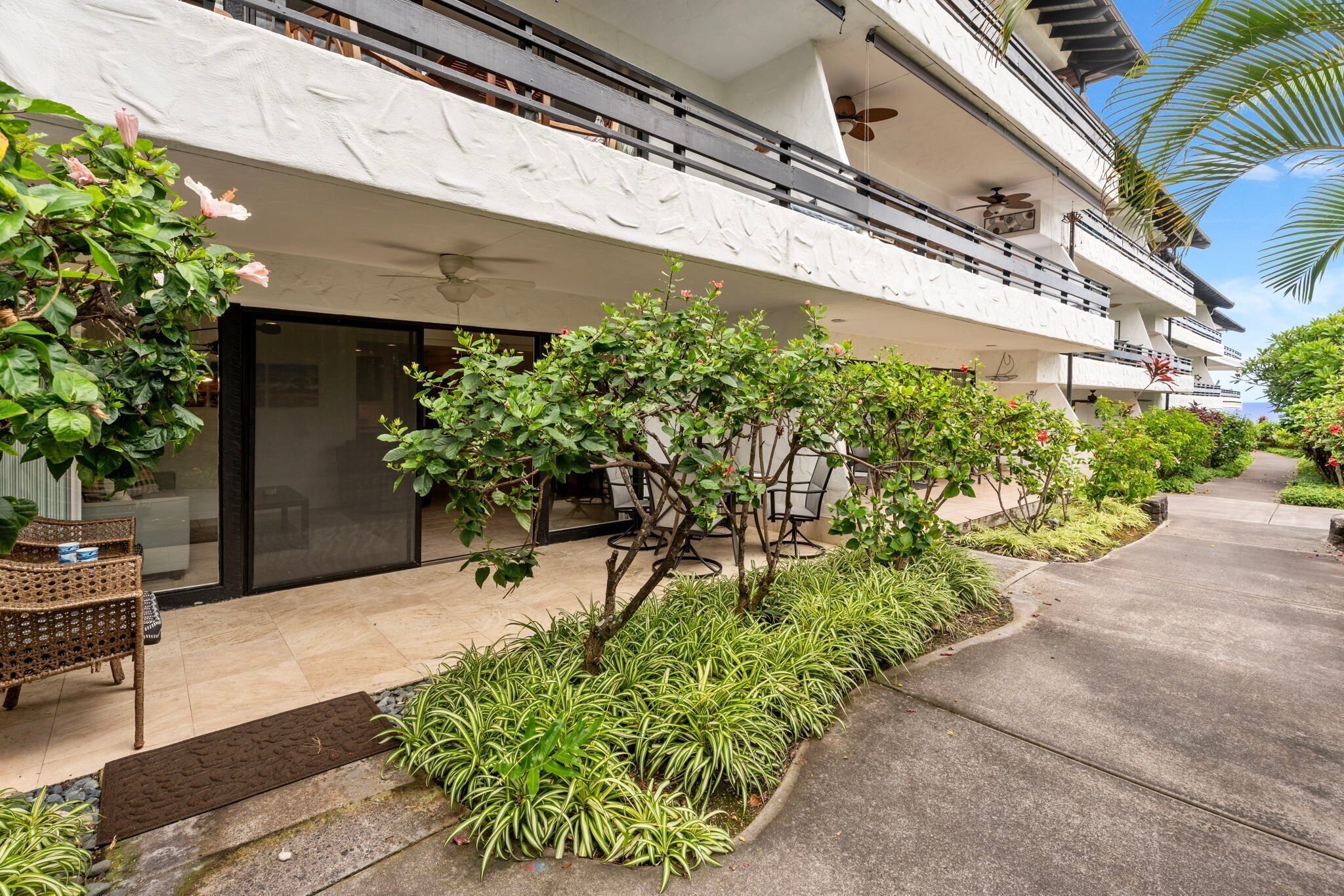 A modern hotel with a balcony, outdoor seating, and lush landscaping.