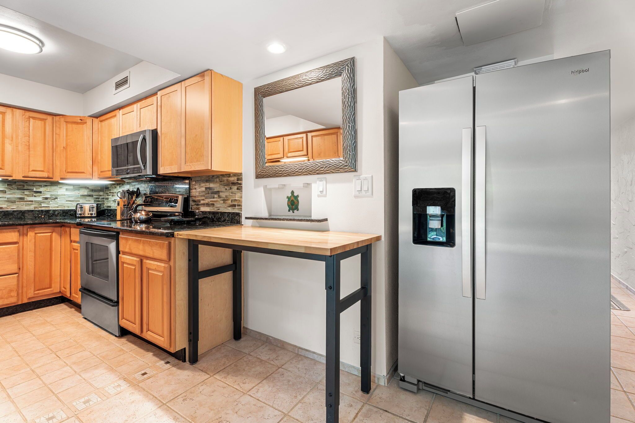 A kitchen with wooden cabinets, a stainless steel refrigerator, a microwave, and a granite countertop.