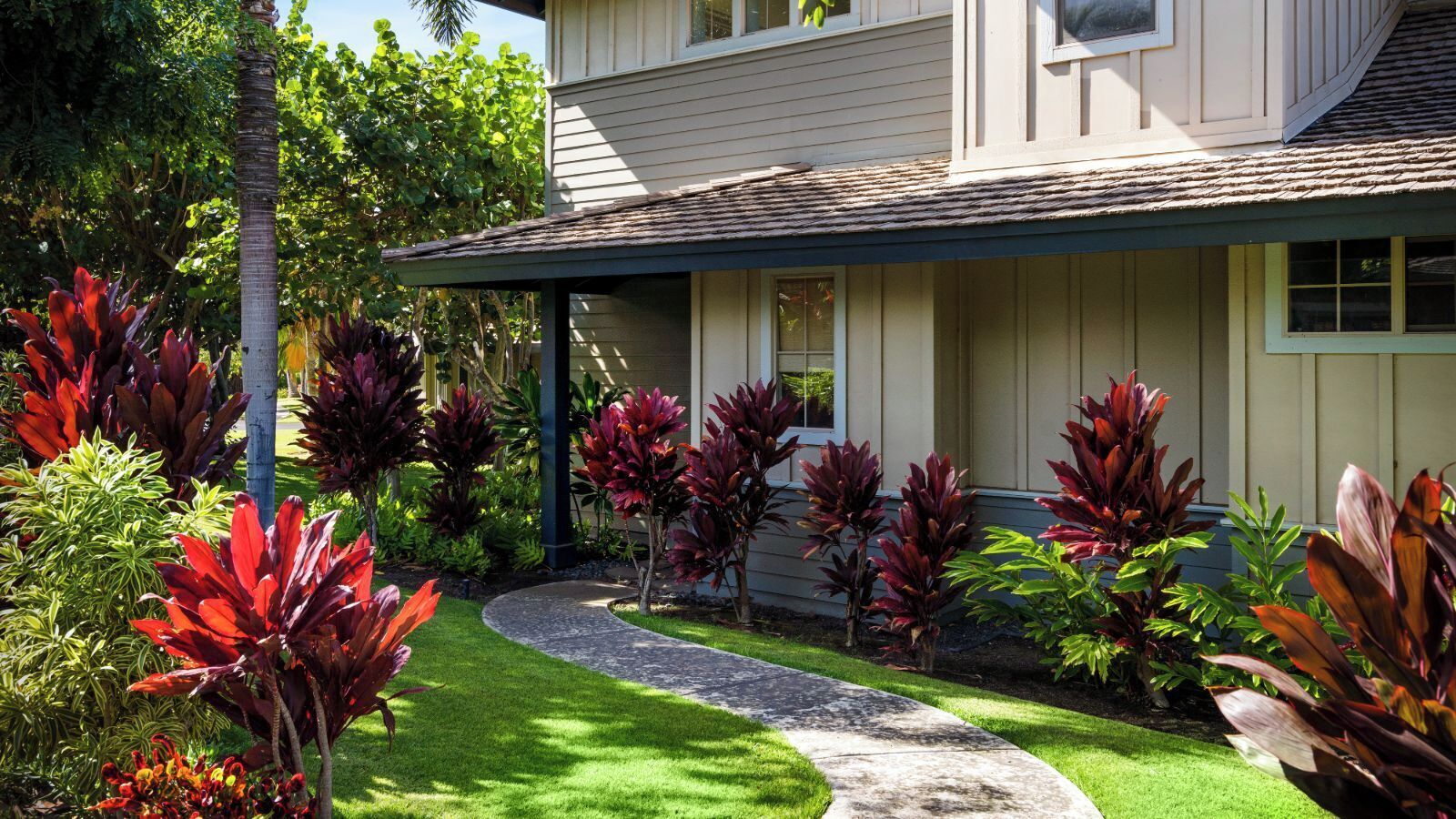 A house with a well-maintained garden, a curved driveway, and a porch with a railing.