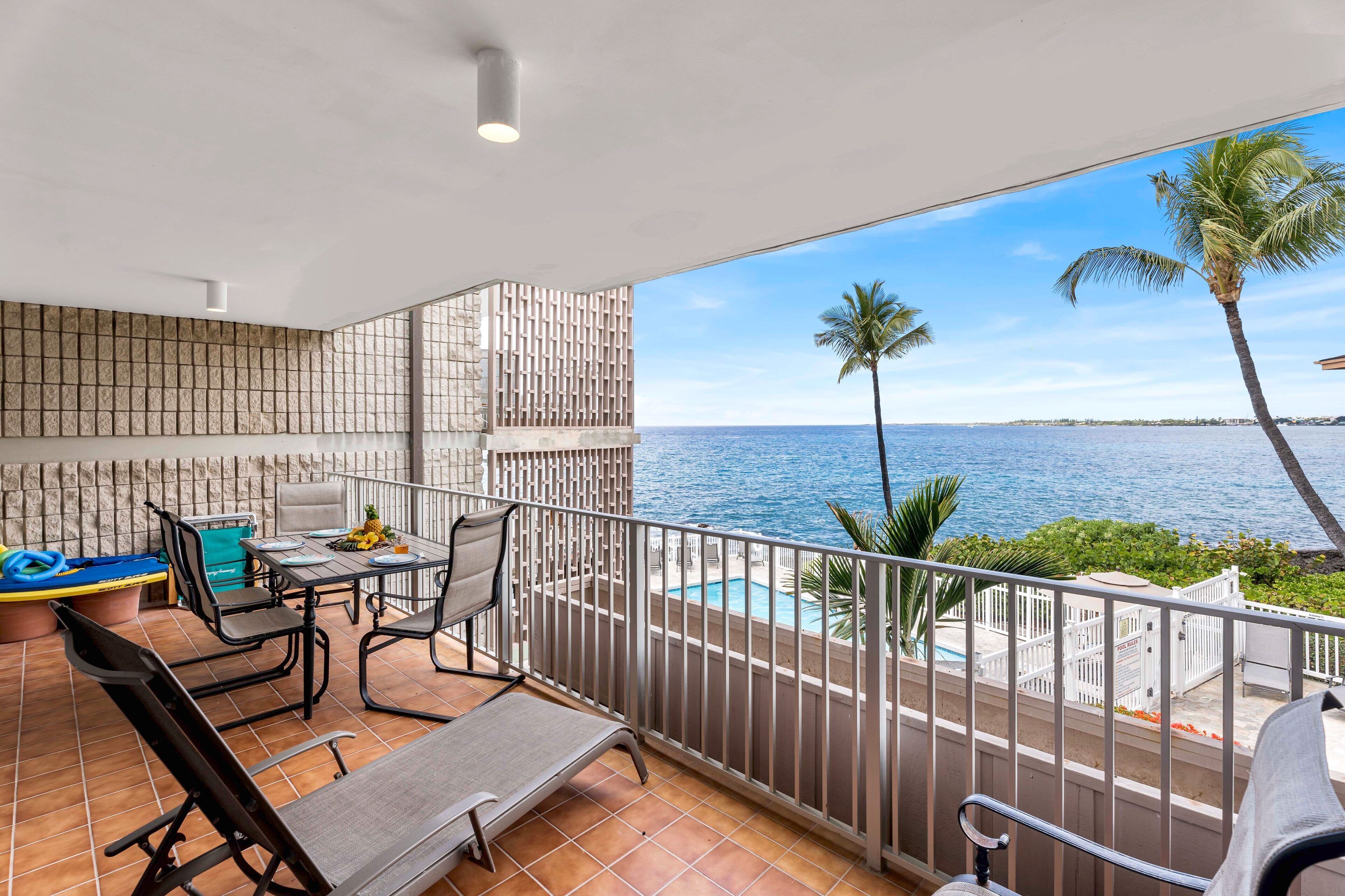 A balcony with a view of the ocean, a pool, and palm trees.