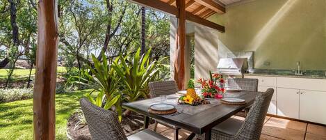 An outdoor patio with a table set for dining, surrounded by wicker chairs, and a kitchen area with a grill.